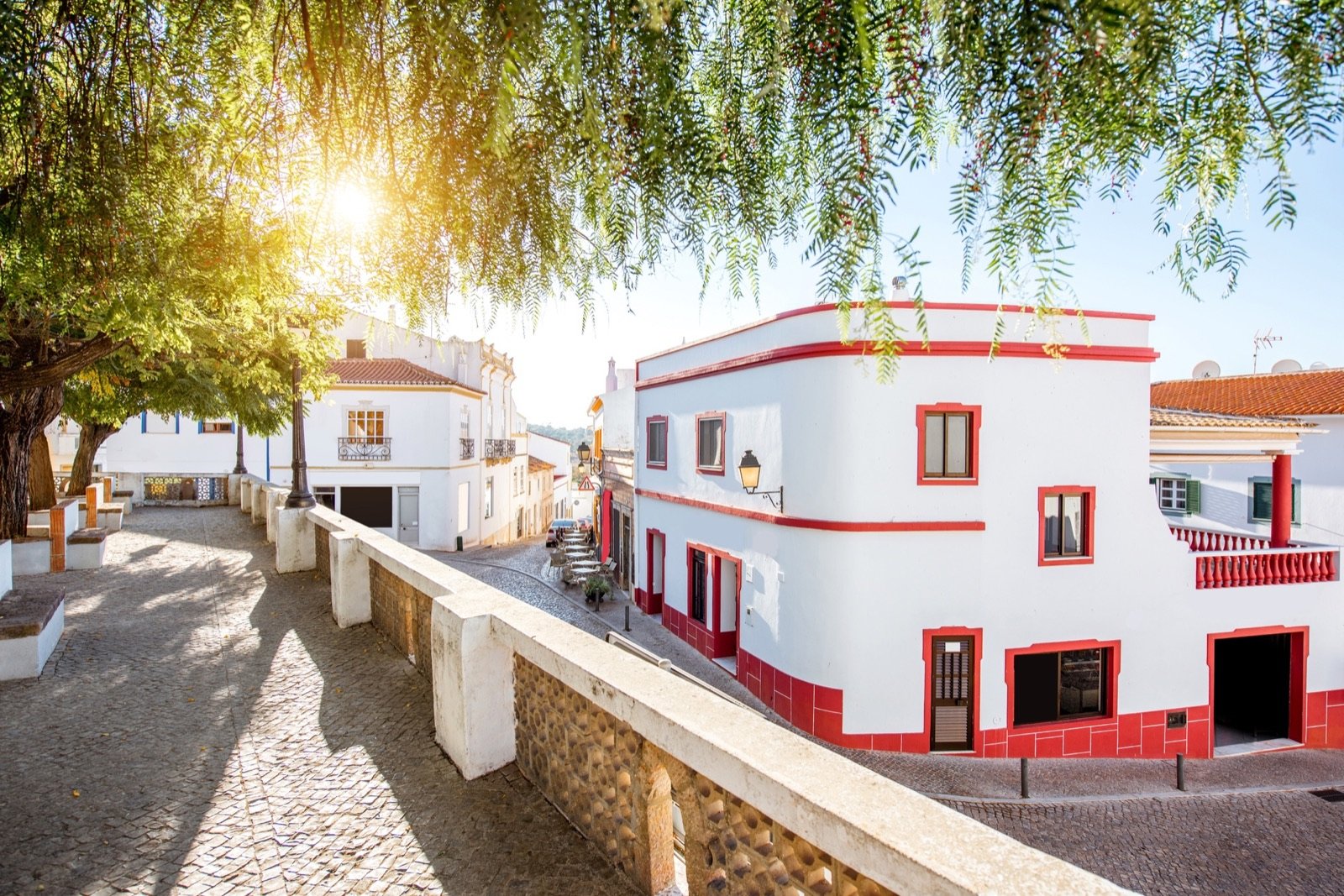 Rua calcetada de Alte com casas brancas de barras vermelhas, ao sol do fim da tarde.