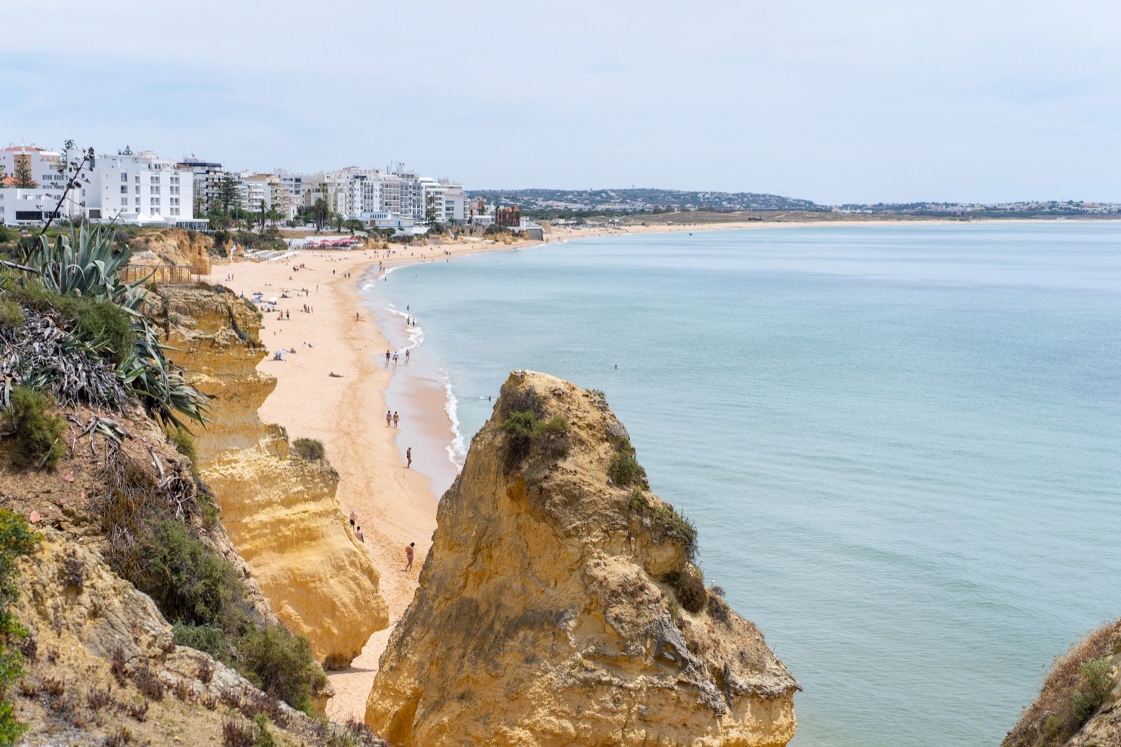 Praia extensa de Armação de Pêra vista da falésia, com prédios de apartamentos ao fundo.