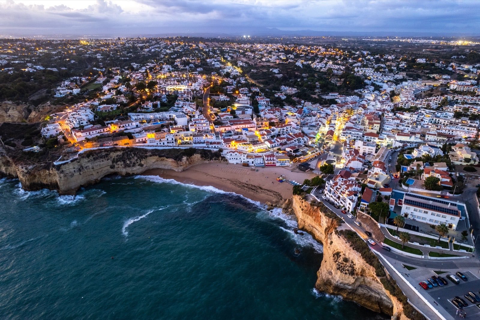Vista aérea ao entardecer das casas brancas de Carvoeiro, sobre a falésia e a praia.
