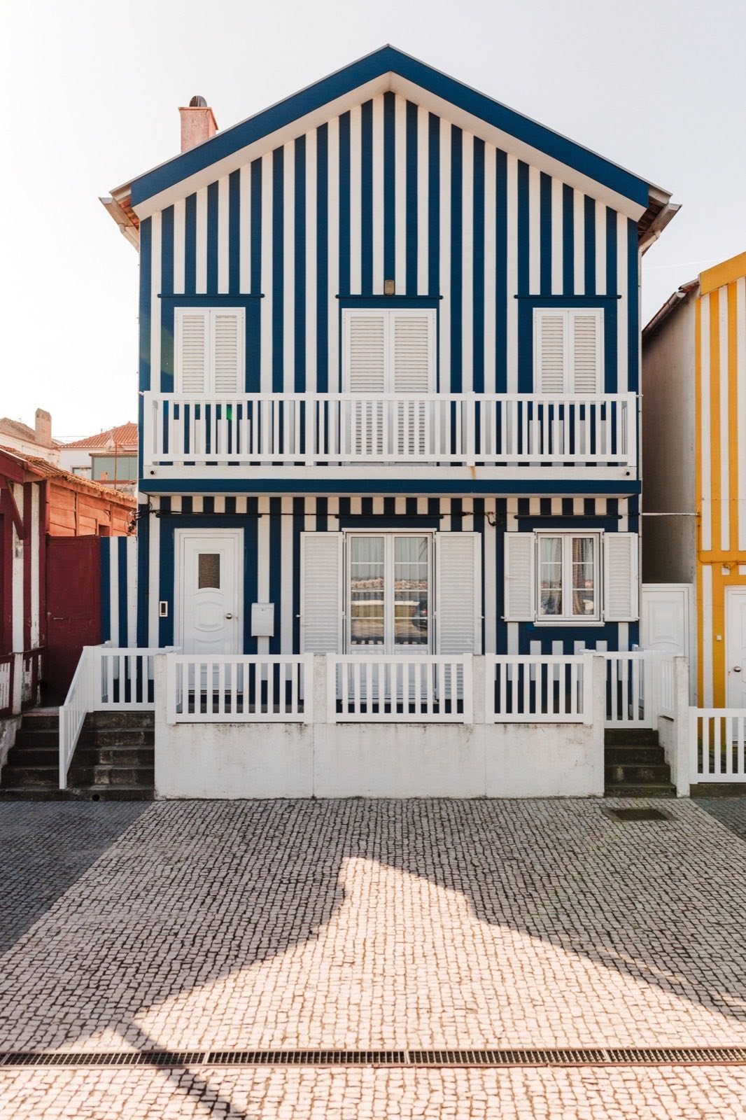 Casa de madeira com riscas verticais azuis e brancas, com varanda, sobre calçada.