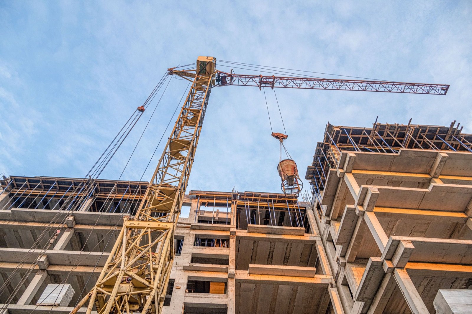 Grua de torre a levantar um balde de betão sobre a estrutura de um prédio em construção.
