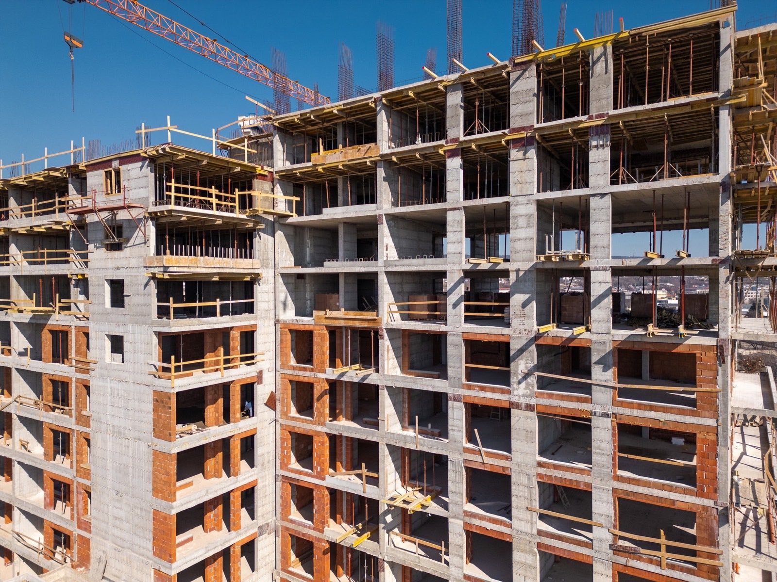 Estrutura de betão de um prédio de vários pisos em construção, com paredes de tijolo por acabar e uma grua.