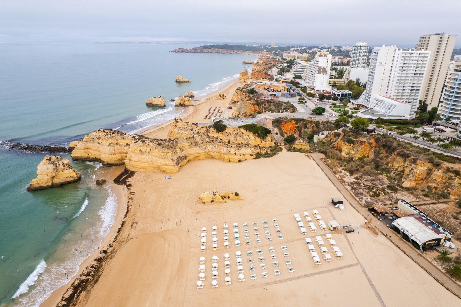 Vista aérea de uma praia extensa em Portimão, com prédios altos de apartamentos no topo da falésia.